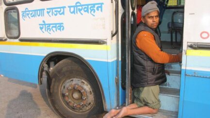 Image showing a person trying to climb into a public bus in India.