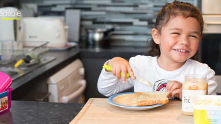 a girl with visual impairment smiling and buttering the toast