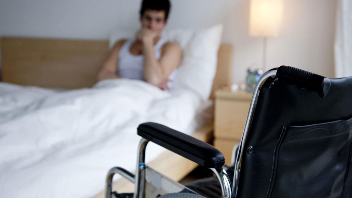 A man sitting on bed staring at his wheelchair. Physical disability can affect mental health of a person.