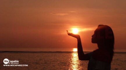A woman posing on a beach as the rising sun appears on her palm.